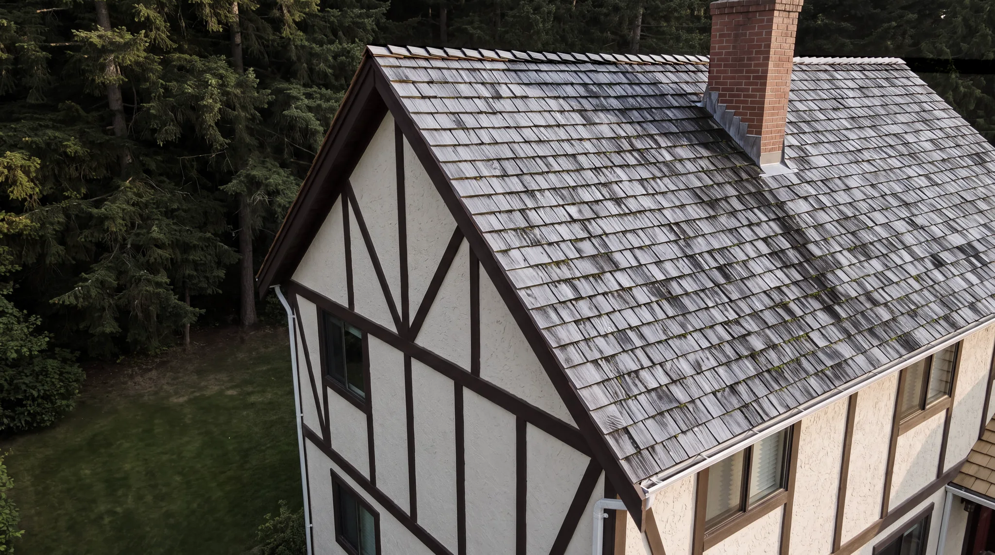 A Tudor-style house with an old, grey, mossy cedar shake roof, seen from above